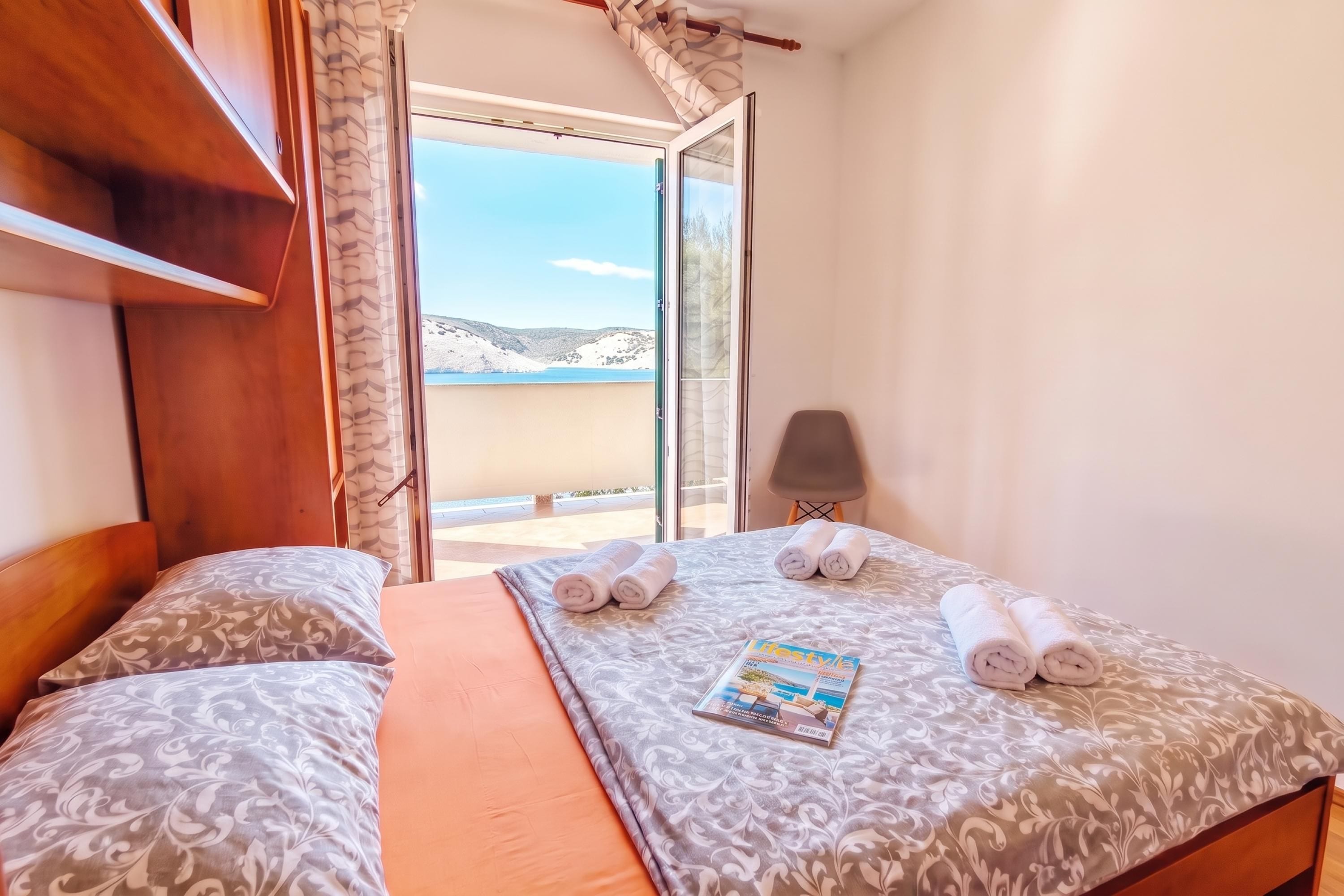 A hotel room with a bed, a window with a view of the sea, and a magazine on the bed.