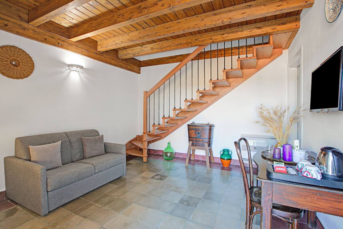 A spacious living area with a wooden staircase, a sofa, and a dining table with various items.