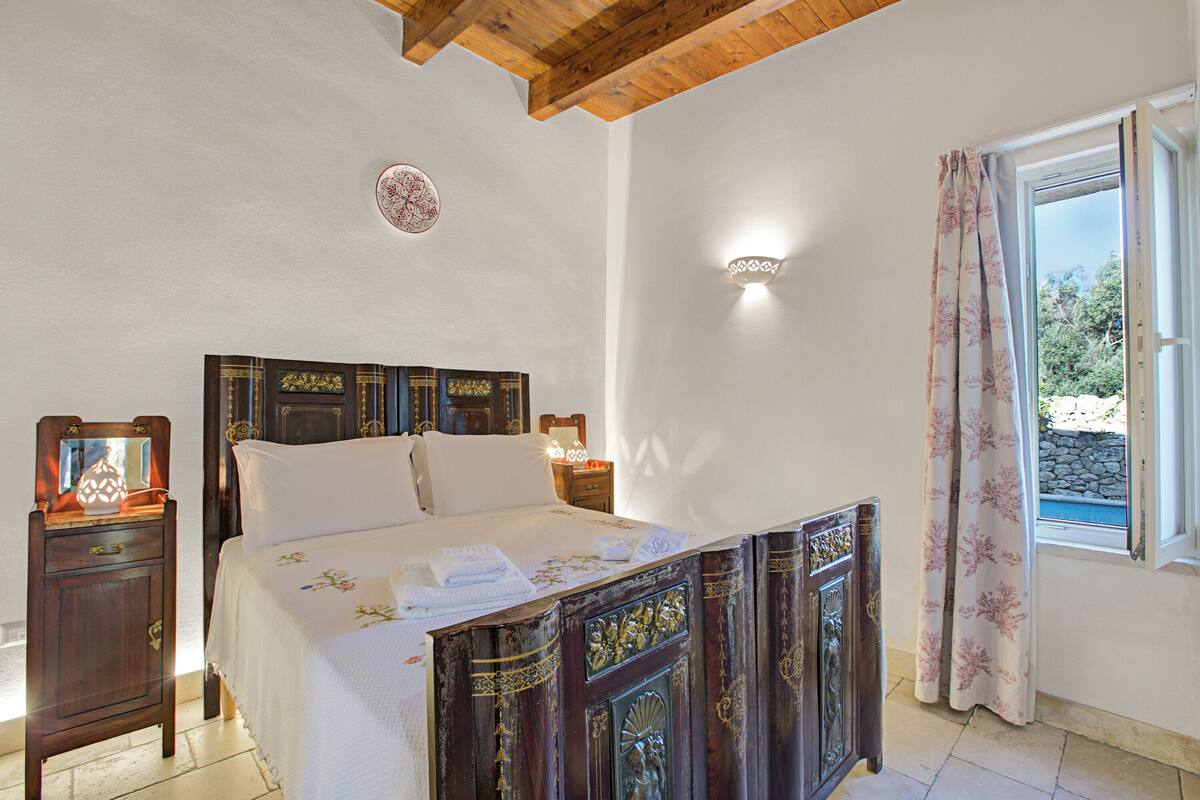 A bedroom with a wooden bed, bedside tables, a nightstand, a wall clock, and a window with curtains.