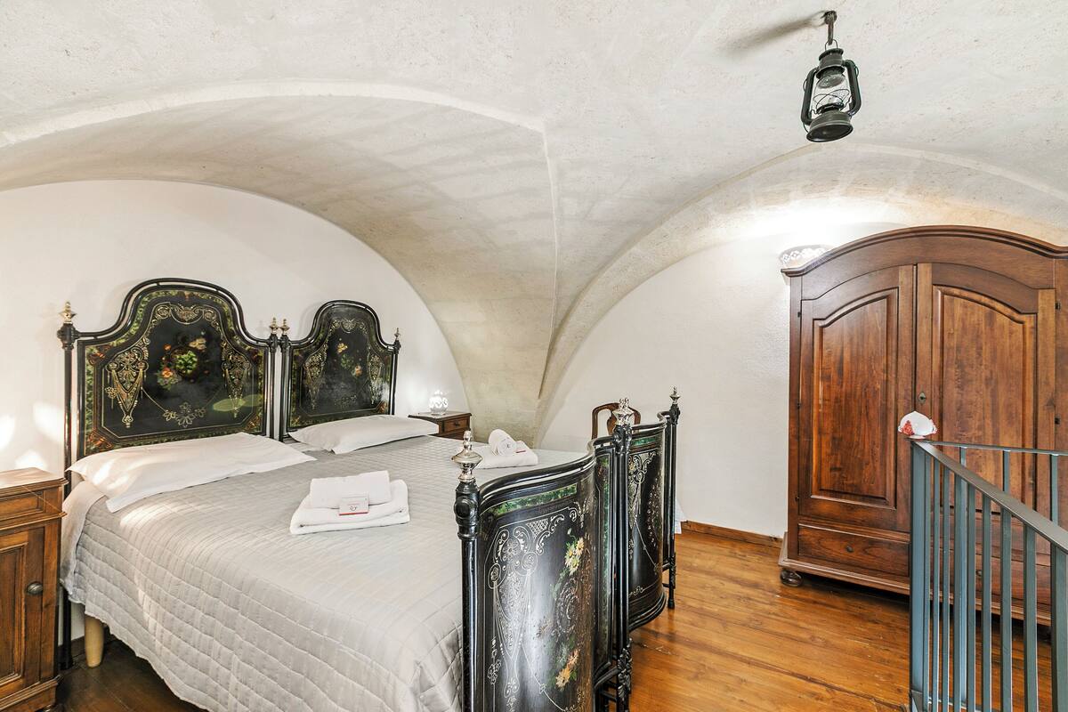 A bedroom with a large bed, wooden wardrobe, and a staircase.
