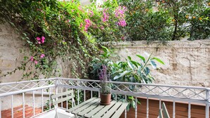 Ein Balkon mit weißem Metallgeländer, einer Holzbank und einem Blumentopf.