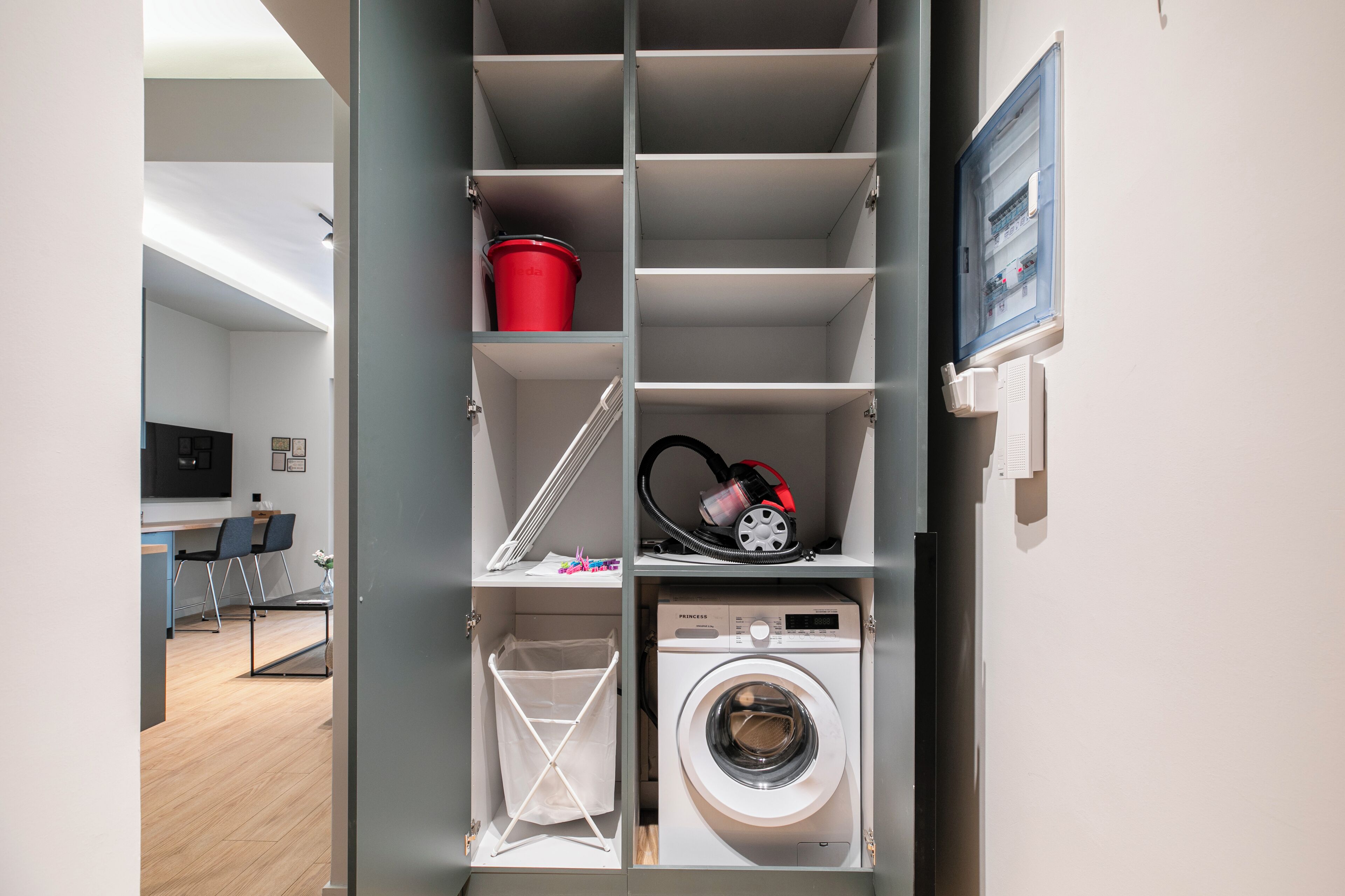 A laundry room with a washing machine, a red bucket, and a vacuum cleaner.