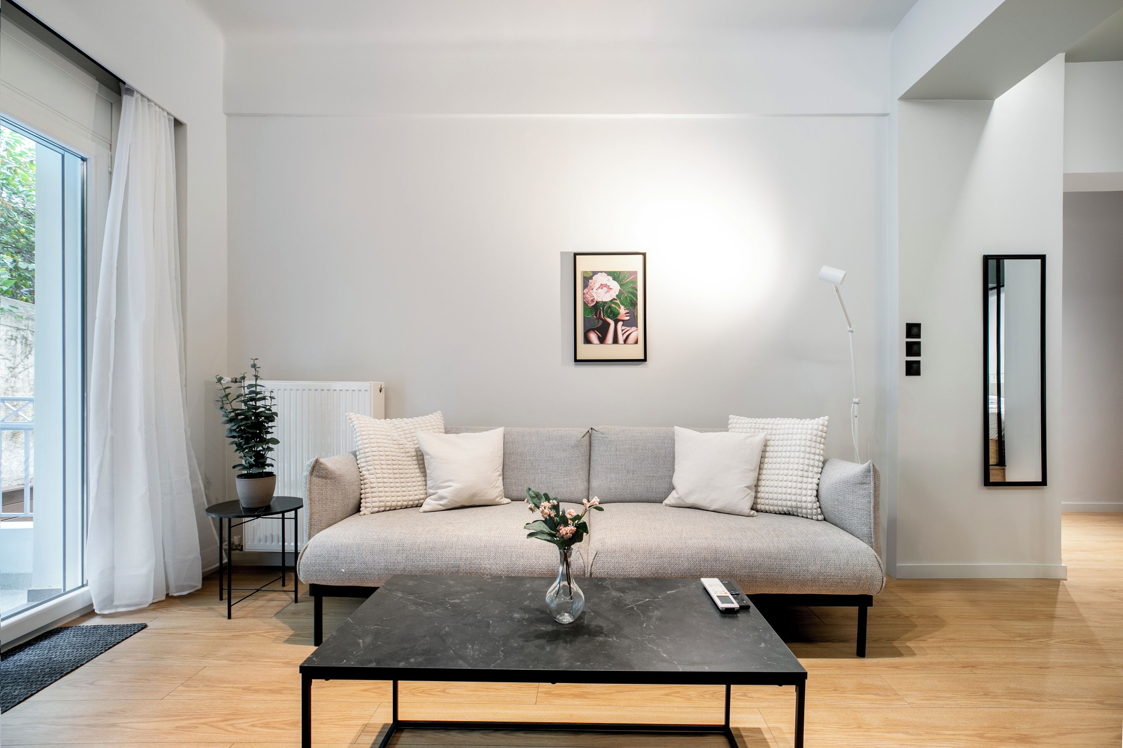 Una sala de estar moderna con un sofá gris, una mesa de centro negra, un cuadro enmarcado en la pared y una planta en maceta.