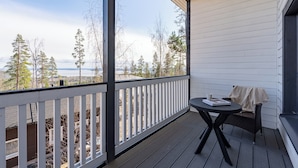 A covered balcony with a white railing, a small table with a chair, and a view of trees and a distant landscape. - Spacious 2BR Cabin at Riihivuori Peak (Muurame)