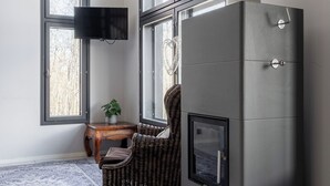 A modern room with large windows, a flat-screen TV mounted on the wall, a built-in fireplace, a wicker chair, and a small wooden table. - Spacious 2BR Cabin at Riihivuori Peak (Muurame)