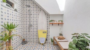 Zona de dutxa petita i emblenada, amb una taula de surf, plantes en testos i una panxa.