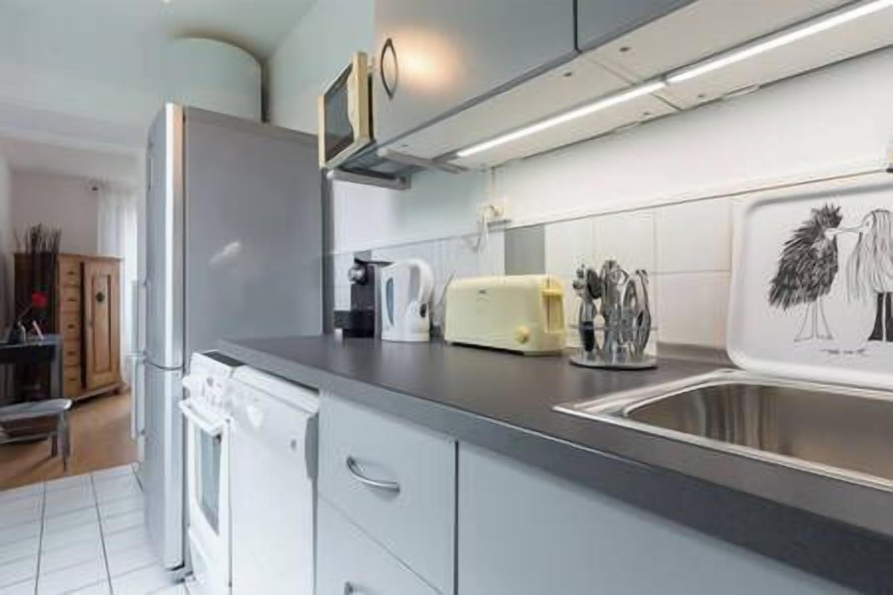 Une cuisine moderne équipée d’un réfrigérateur en acier inoxydable, d’un four encastré, d’un grille-pain et d’un évier agrémenté d’un pare-éclaboussures décoratif.