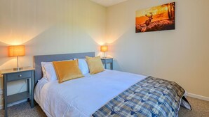 Una cama bien hecha con sábanas blancas y dos almohadillas doradas, flanqueada por dos mesitas de noche con lámparas, en una habitación con un cuadro colgado en la pared.