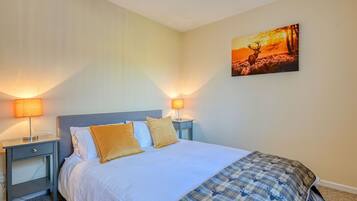 A neatly made bed with white linens and two gold pillows, flanked by two bedside tables with lamps, in a room with a single wall-mounted painting.