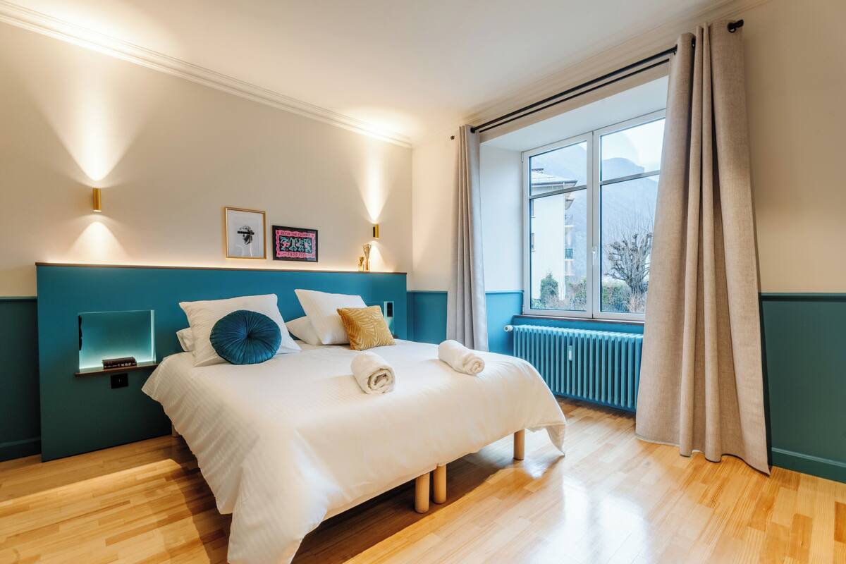 A hotel room with a large bed, a view of the outdoors, and a blue accent wall.