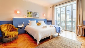 Ein Schlafzimmer mit einem Bett, einem Sessel, einem Fenster und einem Wandregal.