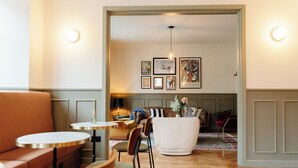 Ein modernes Wohnzimmer mit einer Couch, Sesseln, einem runden Tisch und einem Couchtisch. An den Wänden befinden sich gerahmte Bilder und eine Pendelleuchte.