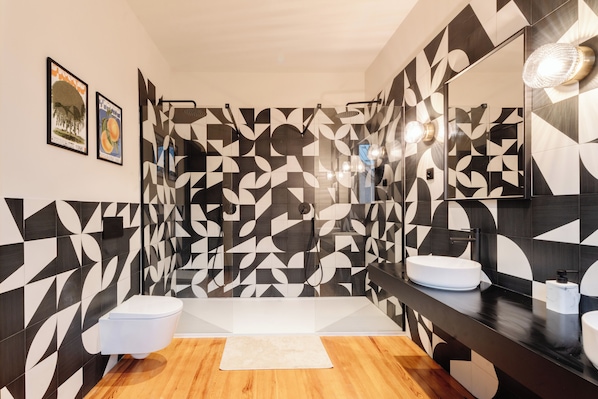 Une salle de bain moderne avec des carreaux aux motifs géométriques, des toilettes blanches, un lavabo avec un miroir et un plancher en bois.