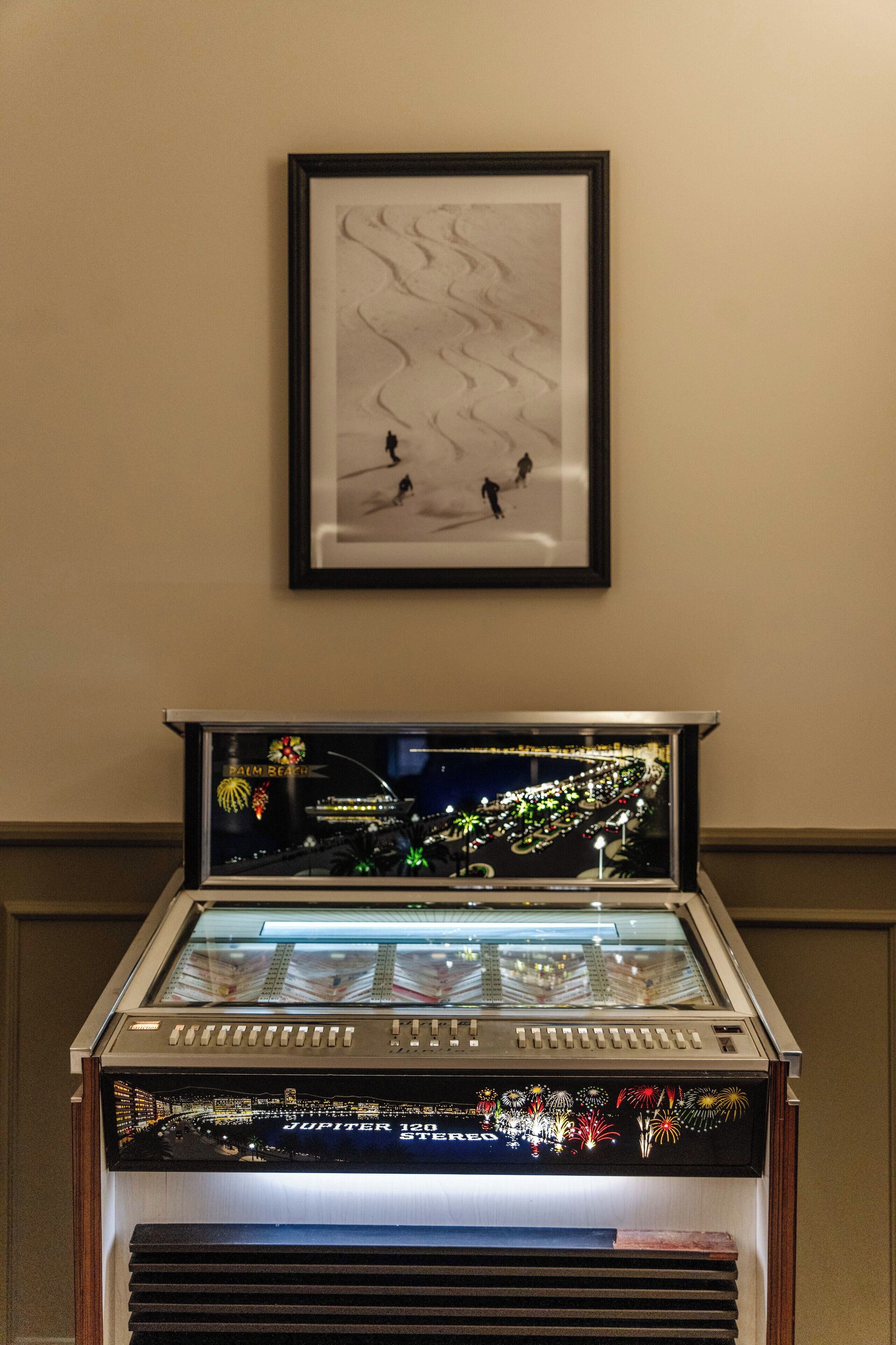 A framed artwork of skaters on ice, a glass display case with a cityscape and fireworks, and a sign indicating "JUPITER 120 ST" above the case.