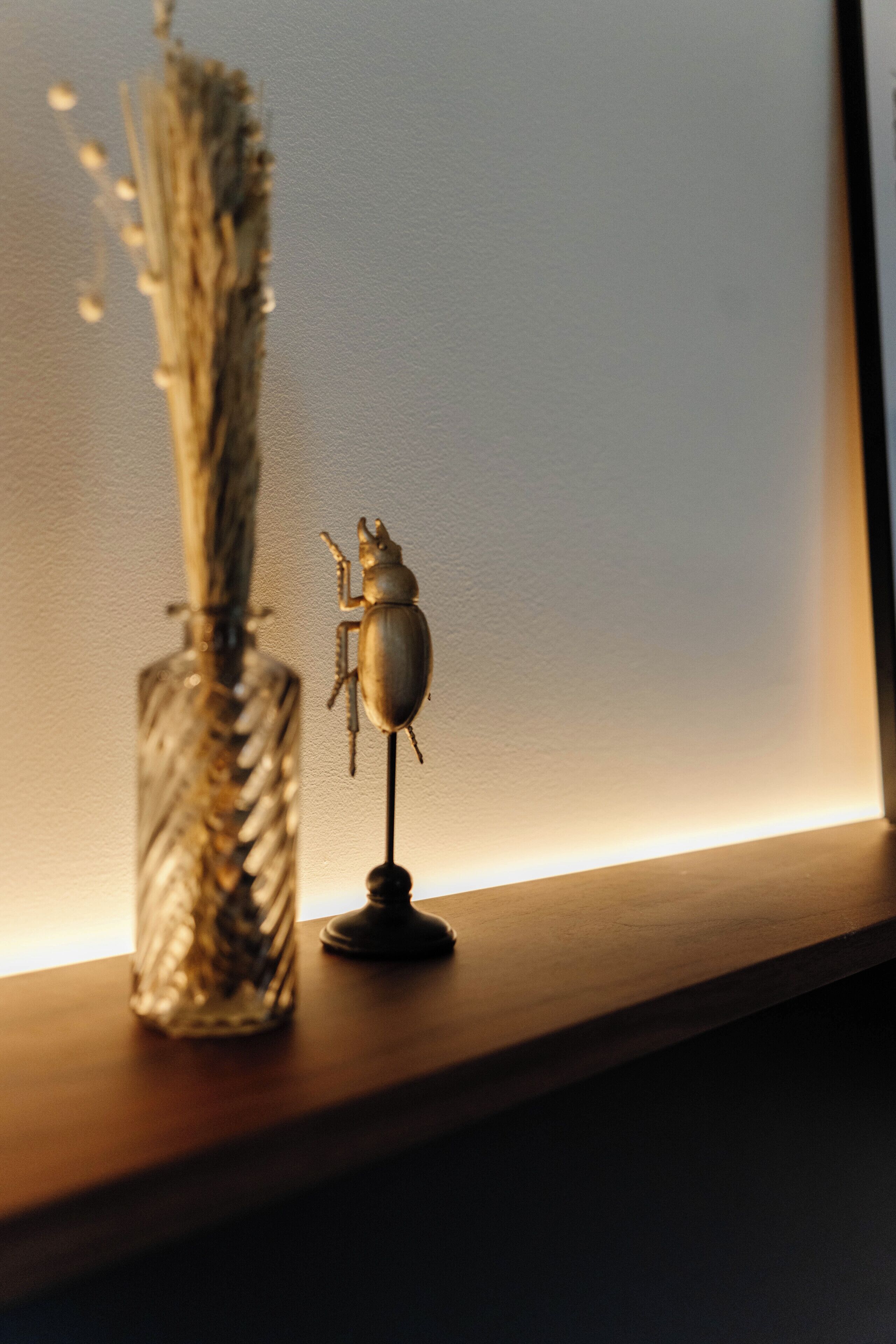 Eine kleine Käferfigur auf einem Regal neben einer Glasvase mit getrockneten Pflanzen.