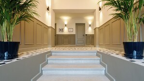 Ein Hotelgang mit Schachbrettmuster, eine Treppe, die zu einer Tür führt, und je eine Zimmerpflanze auf jeder Seite.