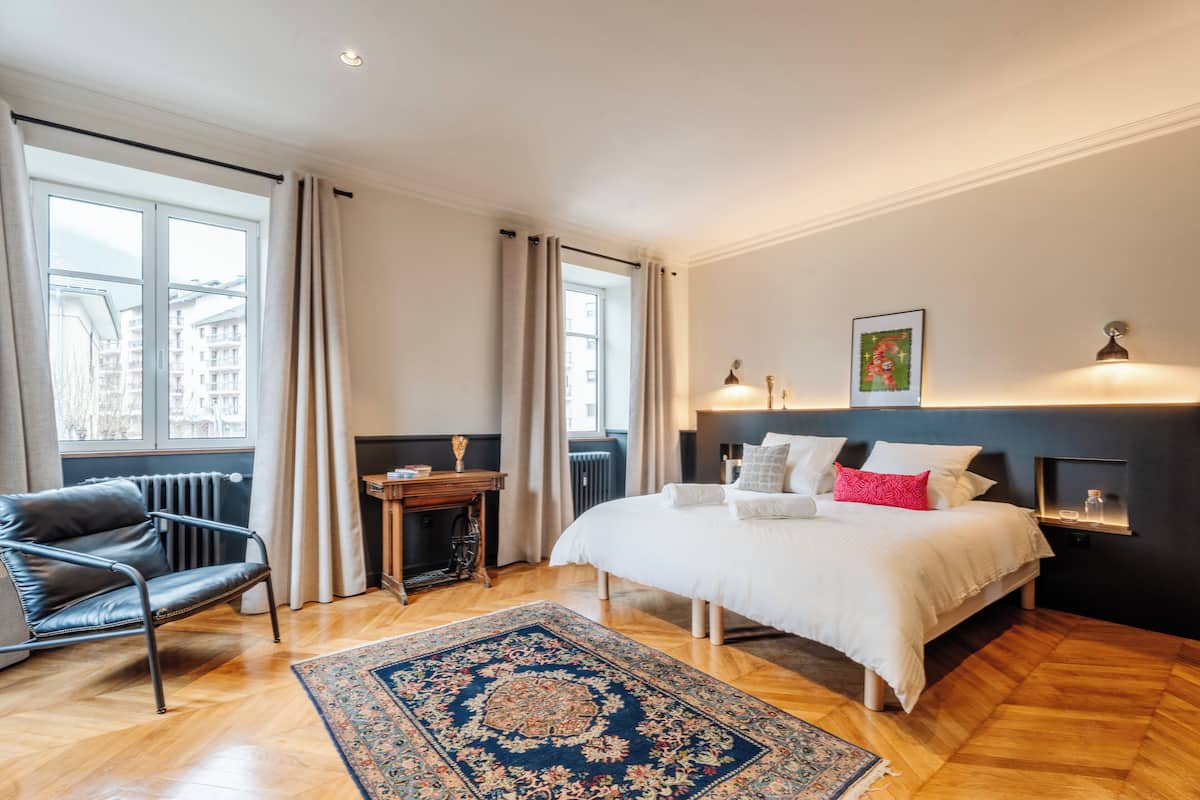 A bedroom with a large bed, a chair, a small table, and a radiator.