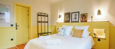 A hotel room with a bed, a bedside table, a wall-mounted light, and a door.