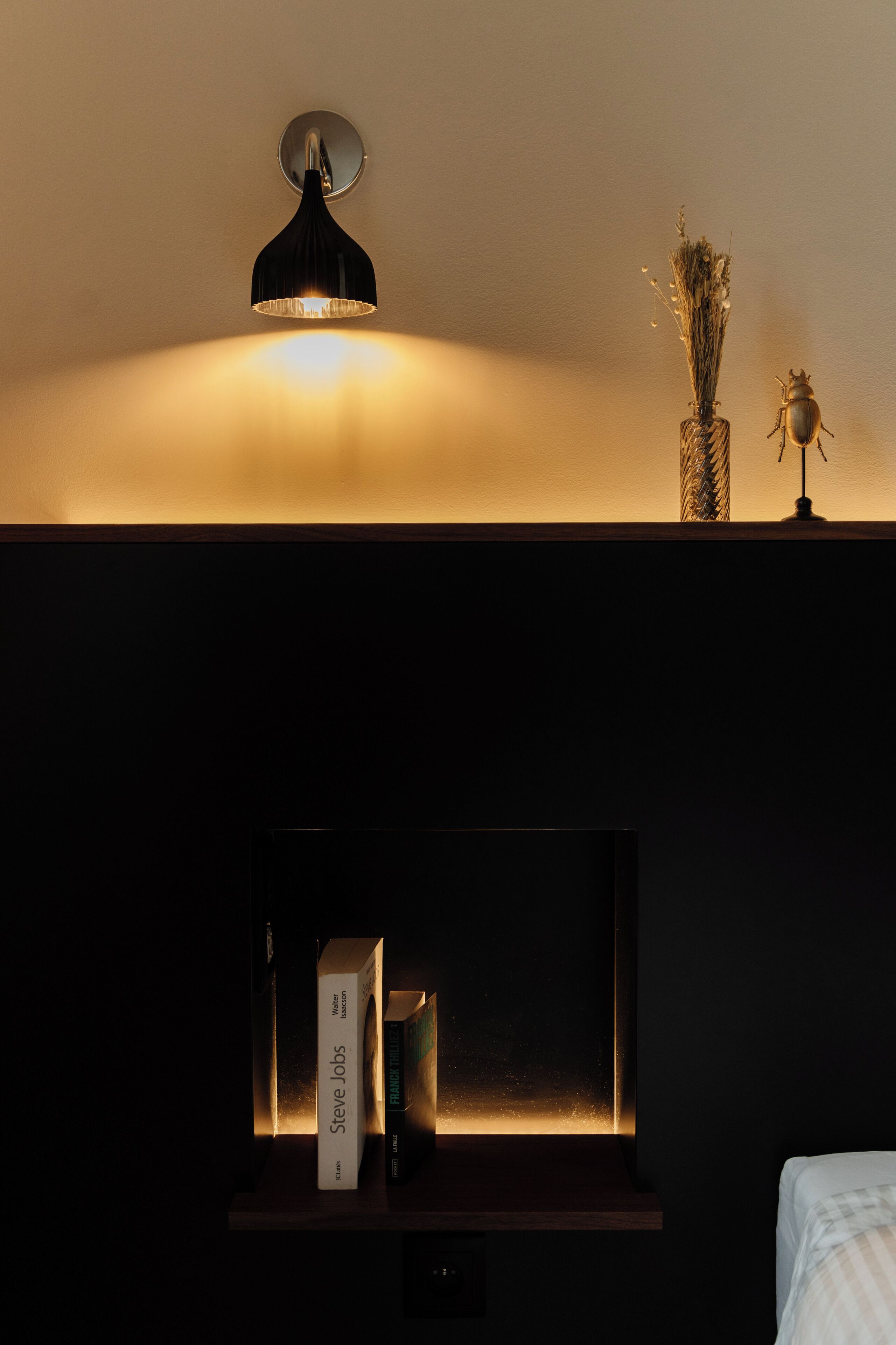 A dark room with a wall-mounted lamp, a small vase with dried flowers, and a framed picture.