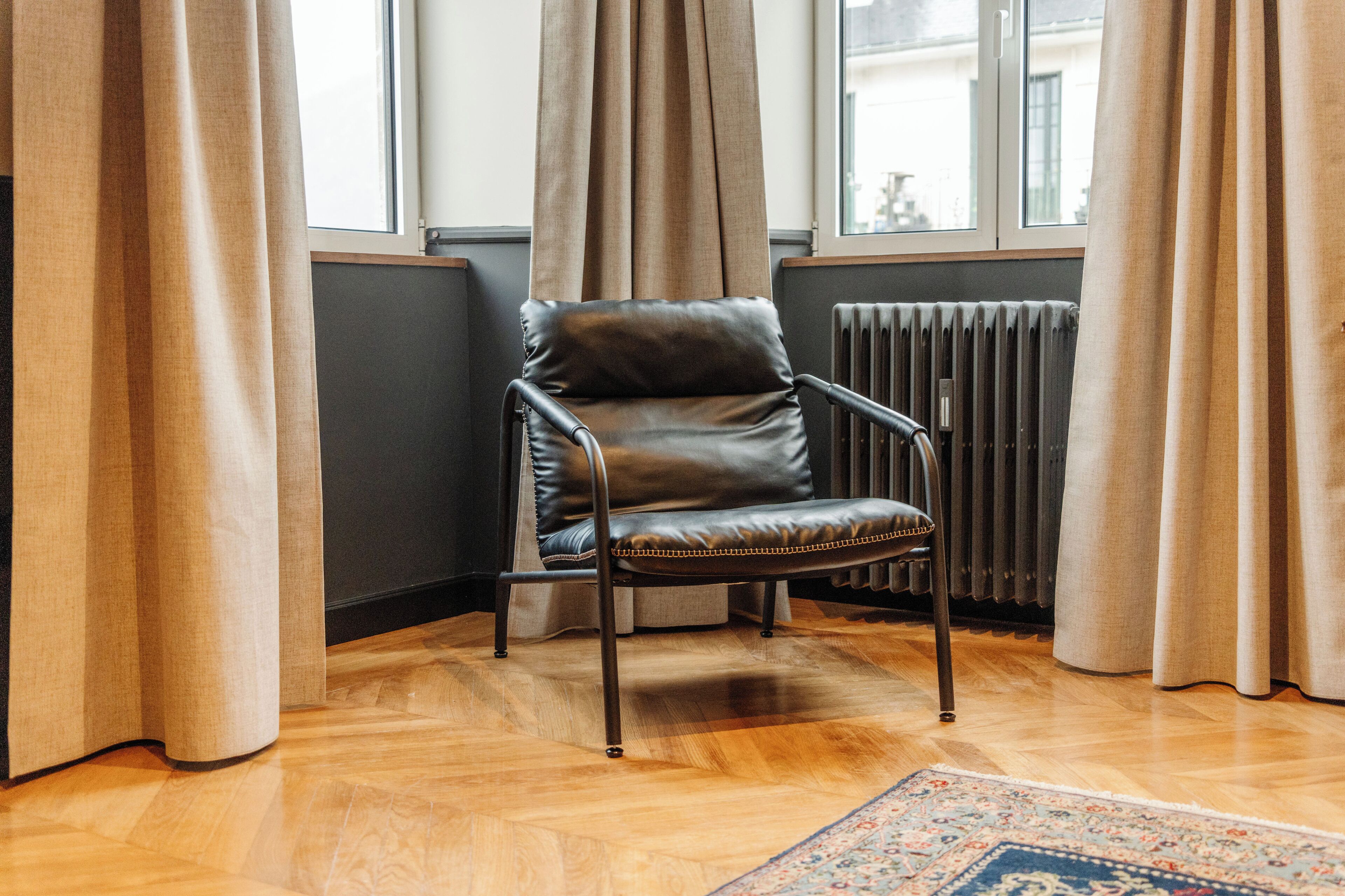 A corner room with a leather chair, wooden floor, and a radiator.