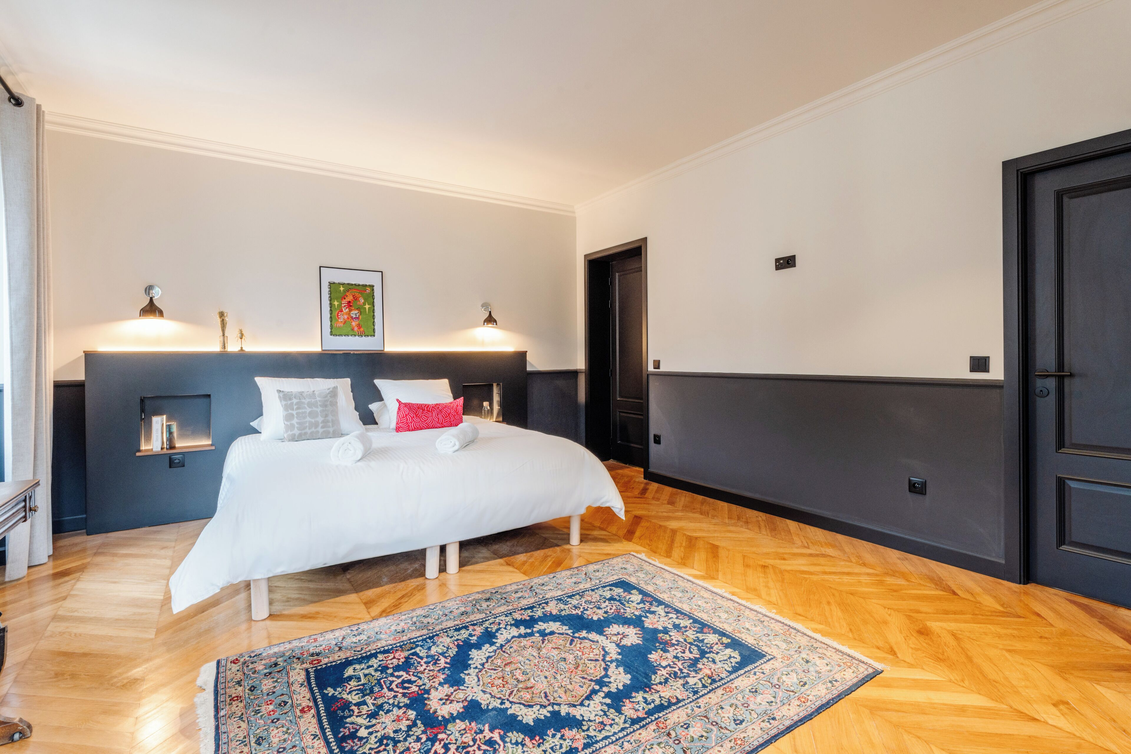 Un dormitorio con una cama grande, un tapete azul y blanco, y dos lámparas fijadas a la pared.