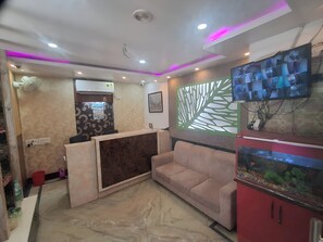 A reception area with a marble floor, a reception desk, a sofa, a fish tank, and a wall-mounted TV. - Roxy Hotel - Near New Digha Beach (Digha)