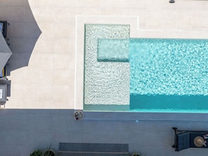 A rooftop pool with clear water, a glass enclosure, and a stone wall.