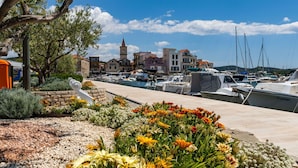 Ein Yachthafen mit vertäuten Booten, eine Kirche mit Turm und eine Steinmauer mit Blumen.