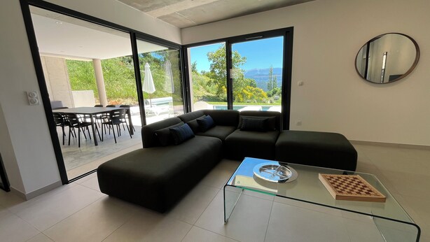 A modern living room with a sectional sofa, a glass coffee table, and a view of a pool and greenery. - Sensation Ventoux, villa in Baronnies provençales (Beauvoisin)