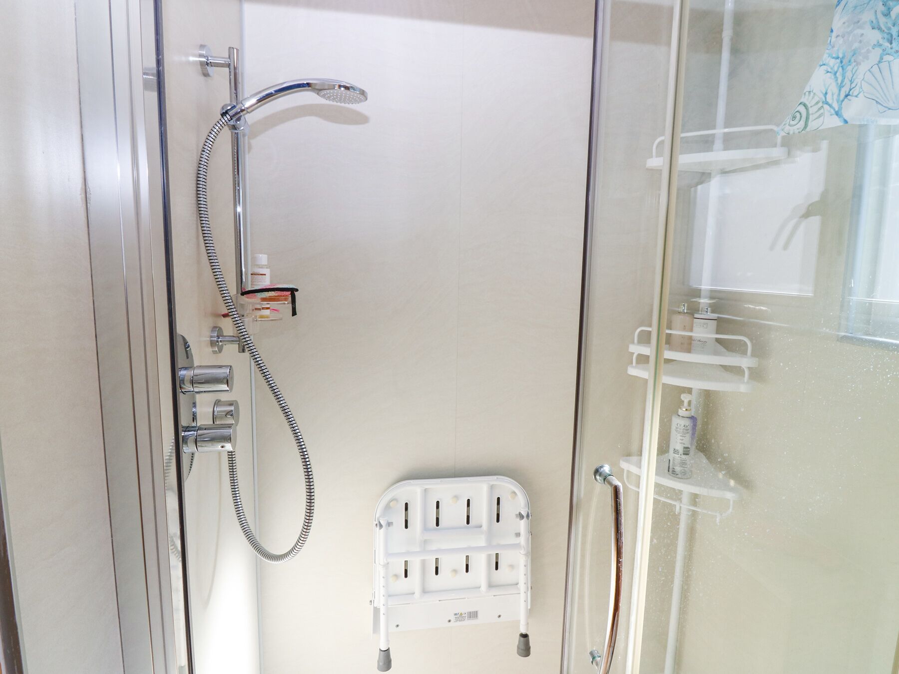A glass-enclosed shower area with a handheld showerhead, a handheld shower attachment, and a white safety step.