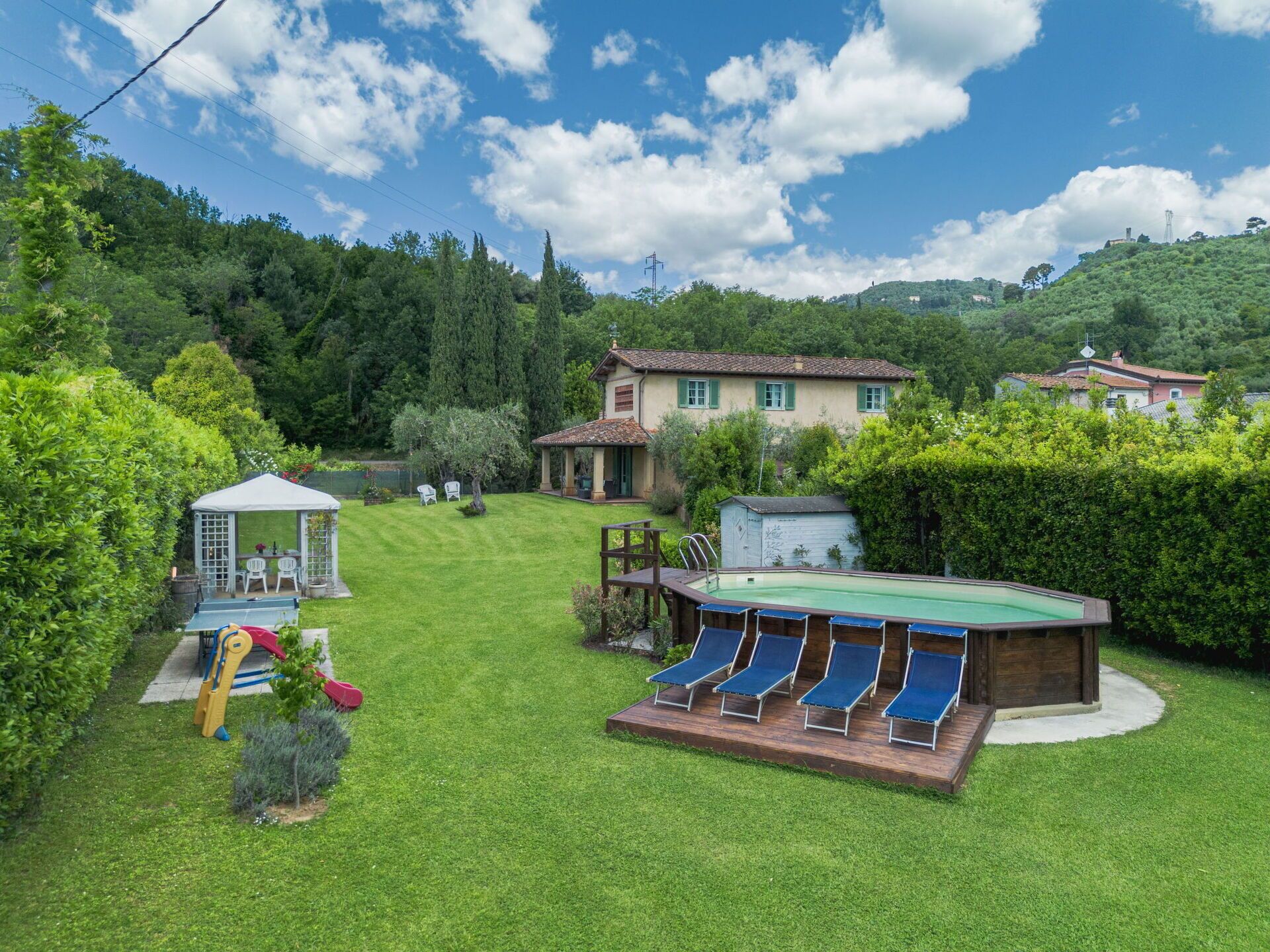A backyard with a swimming pool, lounge chairs, a gazebo, and a small play area.