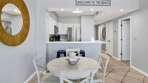 Una cocina moderna con armarios blancos, una isla central y un letrero que dice "WELCOME TO THE BEACH" sobre la isla.
