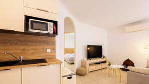 A modern kitchen with a microwave, sink, and a small refrigerator. There is a TV and a wooden cabinet in the living area. - Valras’Loc – Rated apartment with pool & quiet terrace (Valras-Plage)