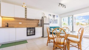 Una cocina moderna con armarios blancos, encimera de madera, horno empotrado y un comedor con sillas de mimbre y una mesa de vidrio.