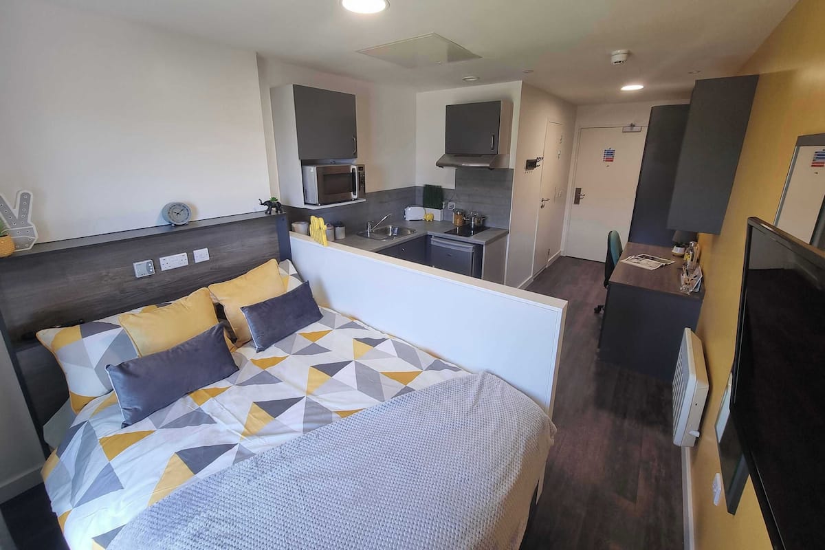A compact hotel room with a bed, a kitchenette, and a TV.