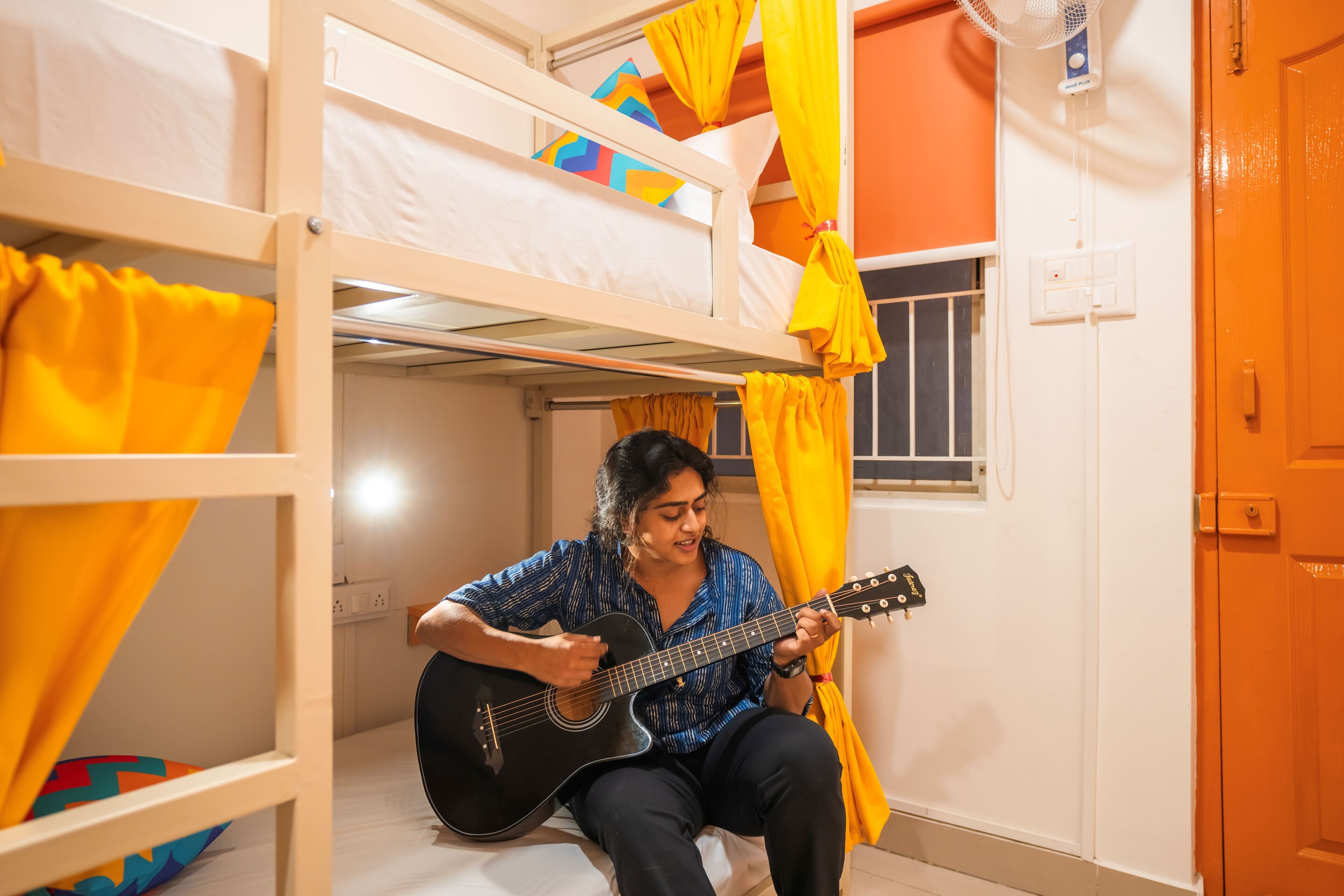 A bunk bed room with yellow curtains and a person playing a guitar.