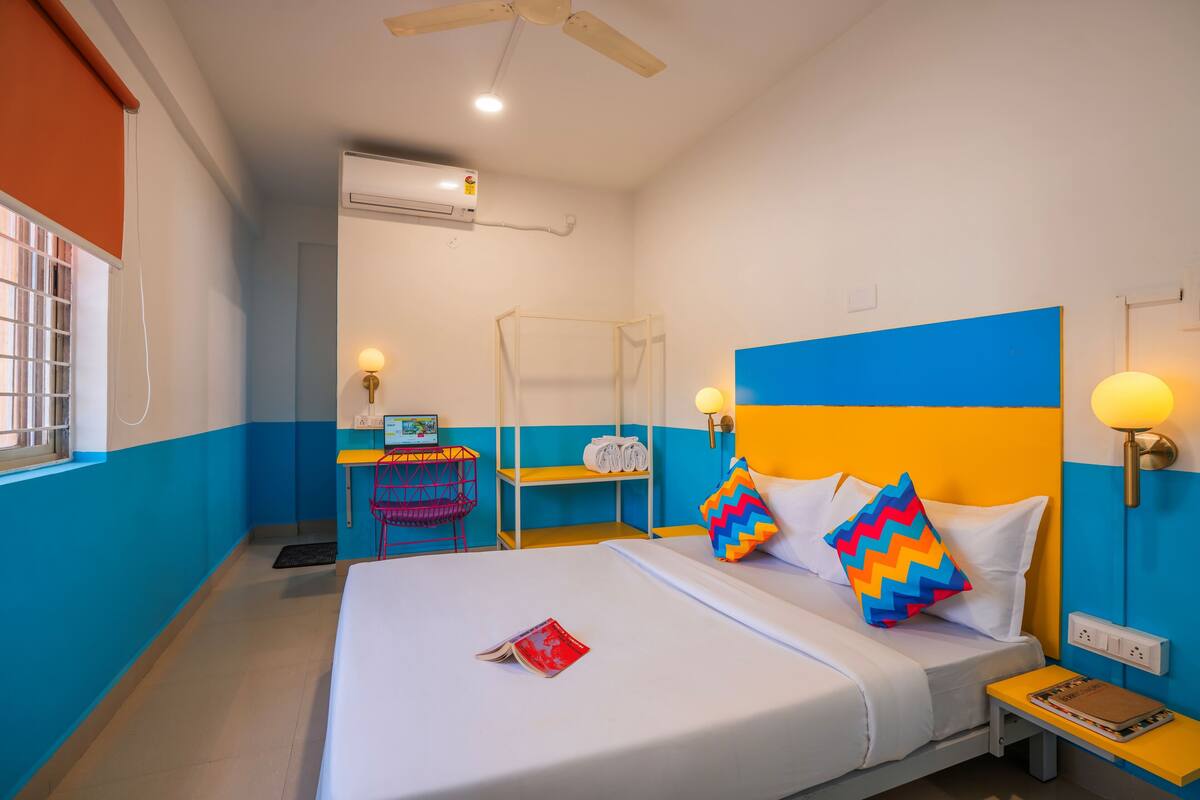 Una camera d'albergo con un letto, un comodino e una scrivania con una sedia.