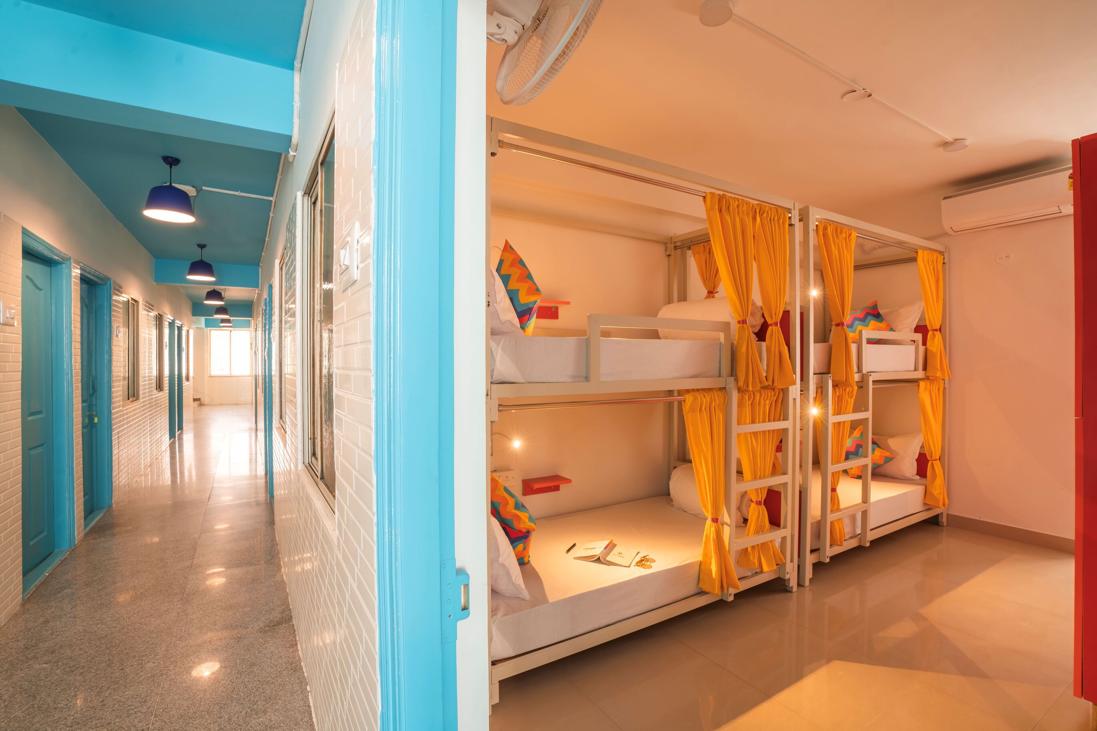 Un couloir d’hôtel avec des lits superposés, un ventilateur et une fenêtre avec des rideaux.
