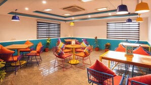 A dining area with tables and chairs, ceiling lights, and a blue accent wall. - goSTOPS Bengaluru HSR Silk Board (Bengaluru)