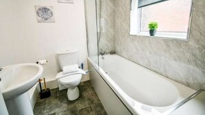 A bathroom with a bathtub, toilet, and sink. There are three framed pictures on the wall. - Comfortable house in Hartlepool (Hartlepool)