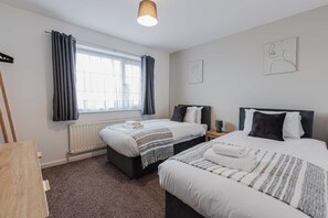 Een hotelkamer met twee bedden, een radiator, een raam met gordijnen, een lamp en een schilderij aan de muur.