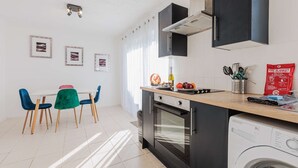 Een moderne keuken met een ingebouwde oven, een wasmachine en een eethoek met blauwe stoelen.