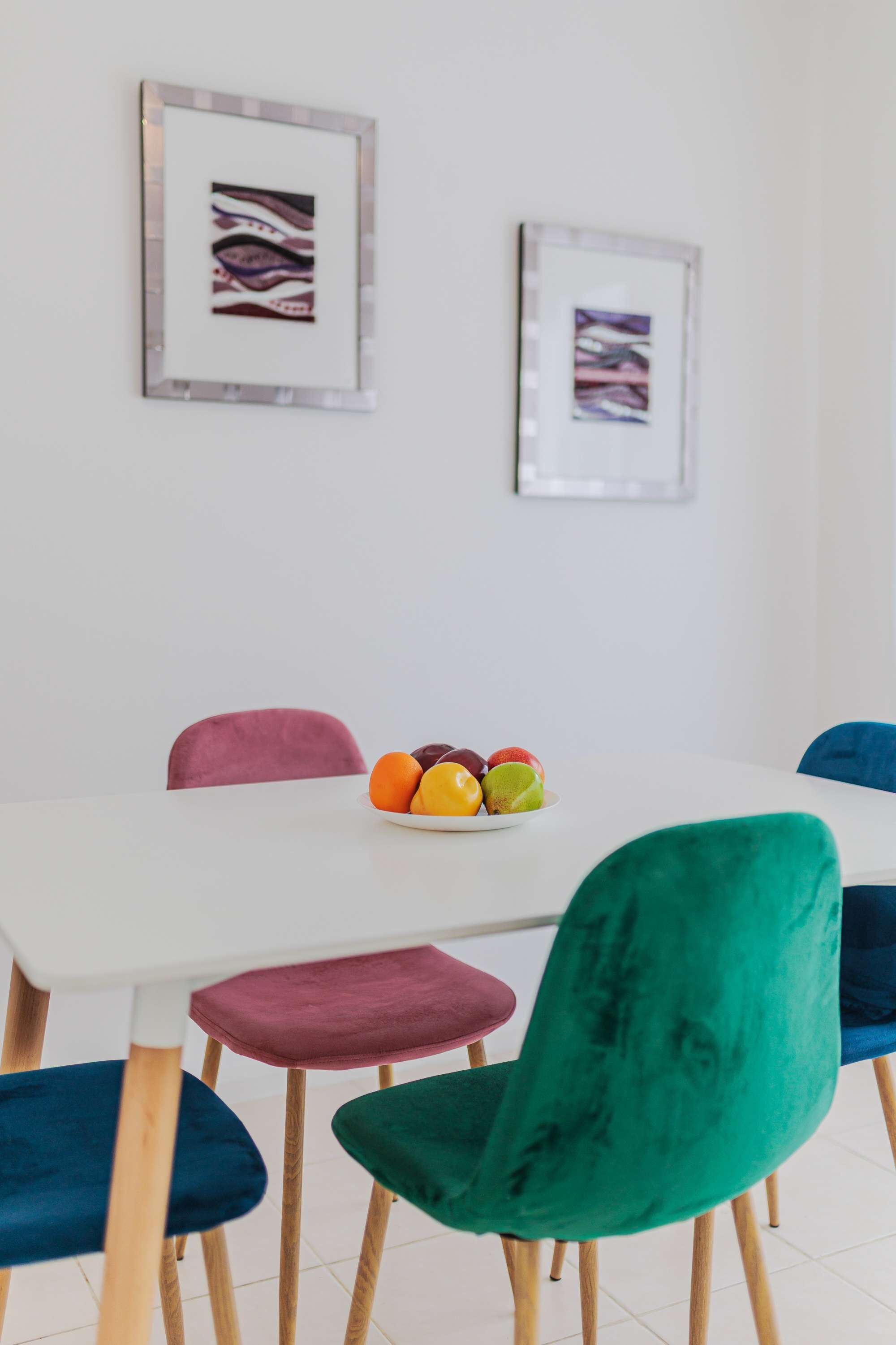 A dining area with a white table, colorful chairs, and a plate of fruit.