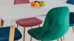 Een eethoek met een witte tafel, kleurrijke stoelen en een schaal fruit.