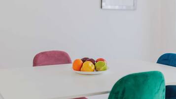 A dining area with a white table, colorful chairs, and a plate of fruit.