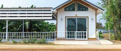 A modern building with a white exterior, a covered area with a metal railing, and a small entrance with a glass door.