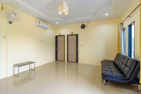 A room with a black leather sofa, a glass-top table, two doors, an air conditioner, and a ceiling fan.