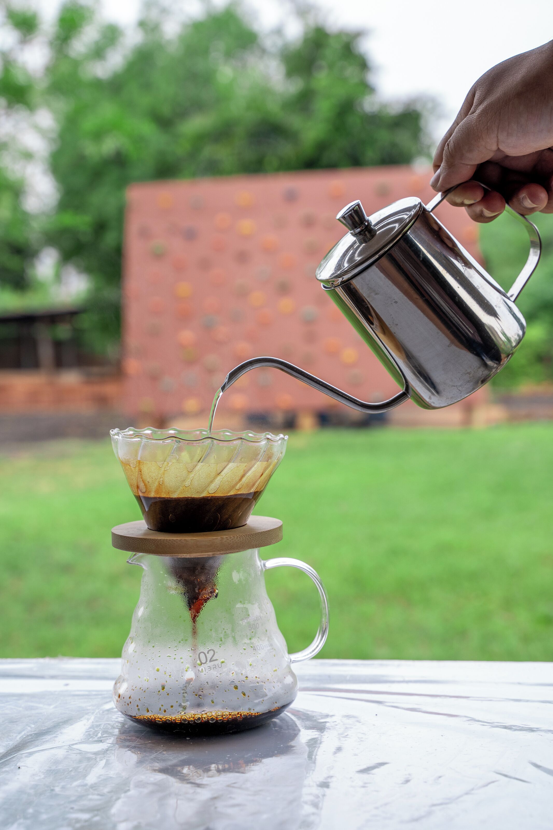 Una mano vertiendo café en una jarra de vidrio con un filtro metálico.