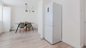 Eine moderne Küche mit einem weißen Kühlschrank, zwei grauen Stühlen, einem Holztisch und einer Pendelleuchte.