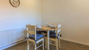 A dining area with a wooden table set for four, four chairs with blue cushions, and a wall clock. - Comfy house in Thornaby, Stockton On Tees (Thornaby on Tees)